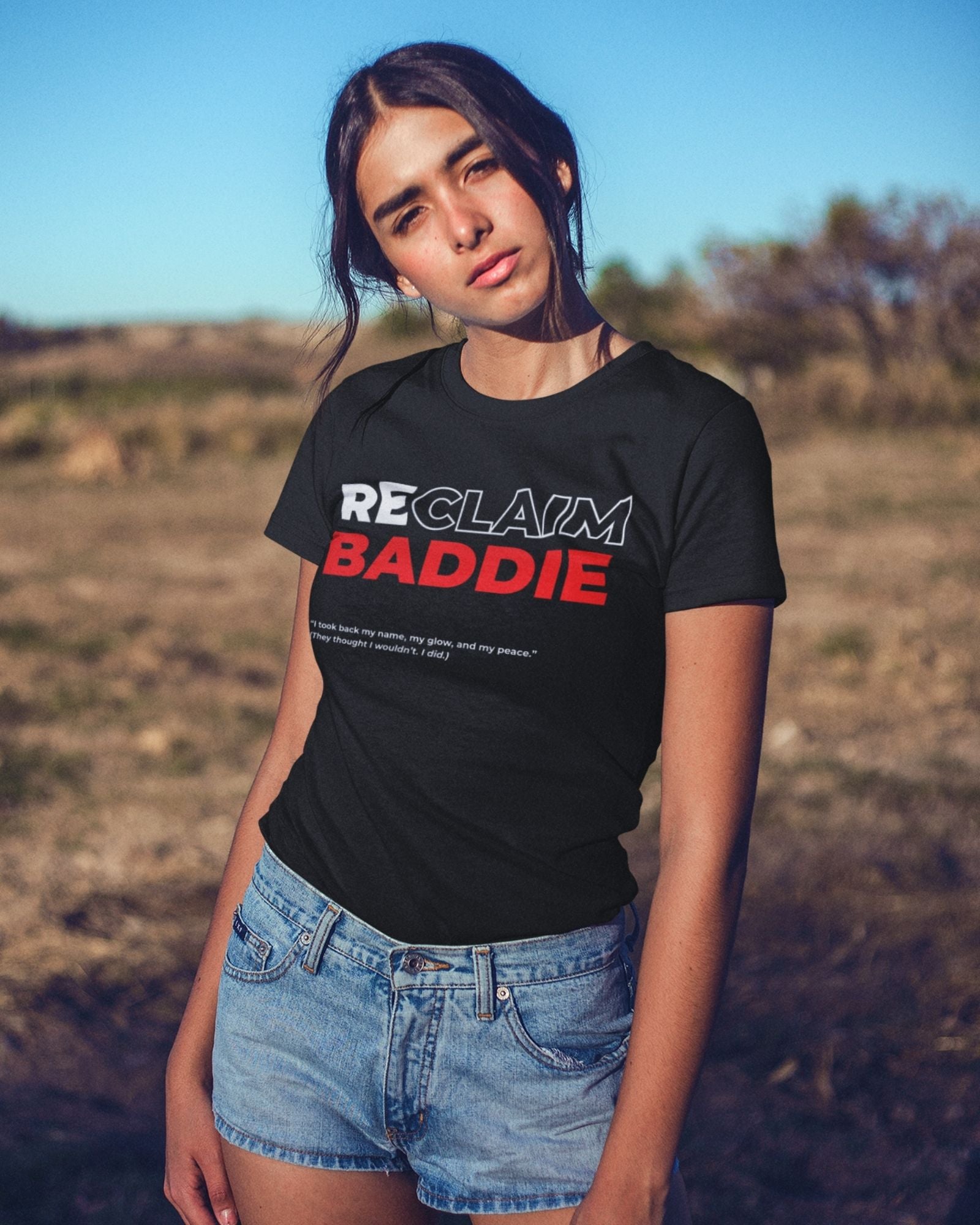 Person wearing a black t-shirt with 'RECLAIM BADDIE' text in an outdoor setting
