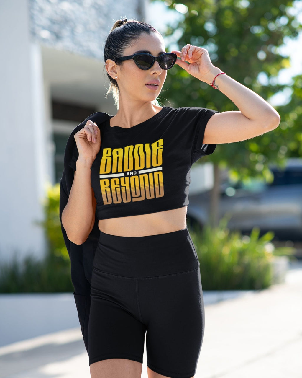 Woman wearing a black crop top with 'Baddle Beyond' text and black shorts outdoors.