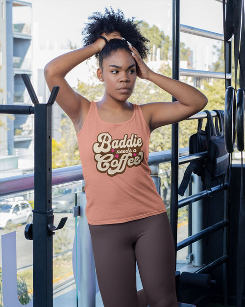 Woman wearing a tank top with 'Baddie needs coffee' text in an outdoor setting.