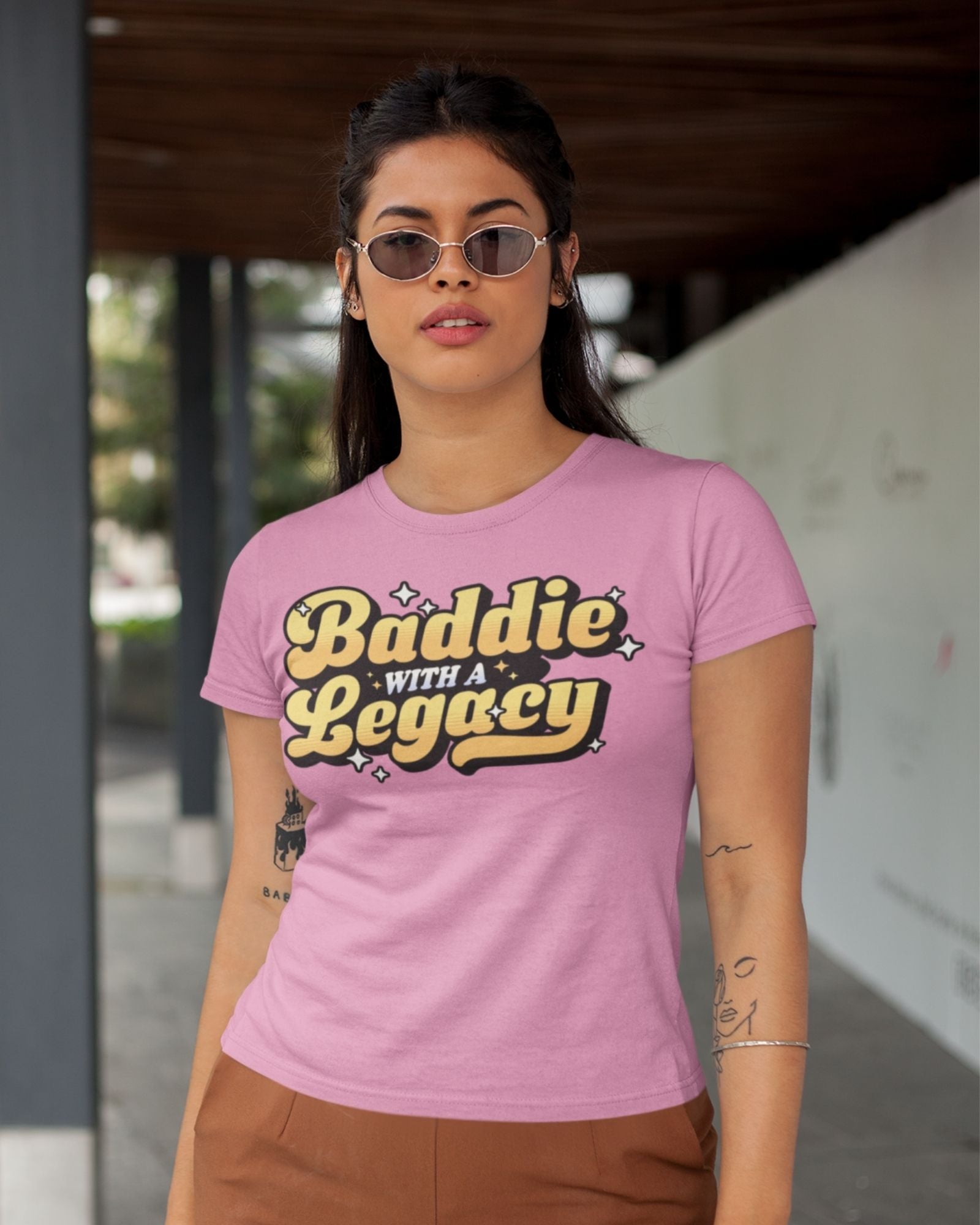 Woman wearing a pink t-shirt with 'Baddie with a Legacy' text.