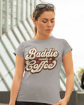 Woman wearing a gray t-shirt with 'Baddie needs a coffee' text.