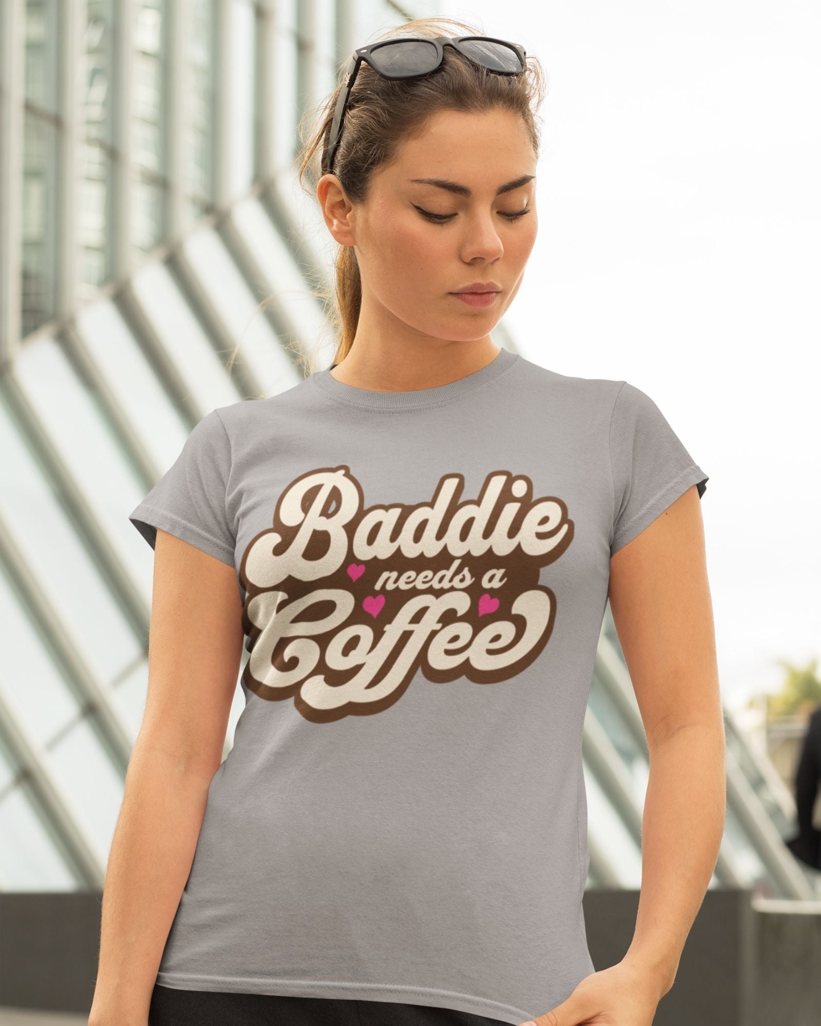 Woman wearing a gray t-shirt with 'Baddie needs a coffee' text.