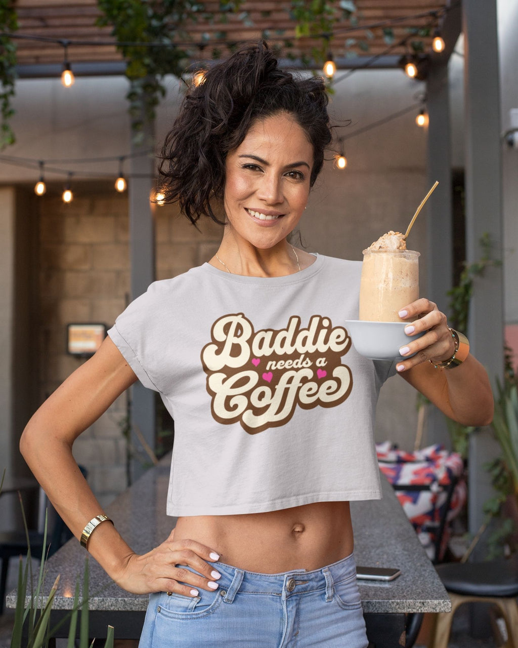 Woman wearing a 'Baddie needs a coffee' shirt holding a drink.