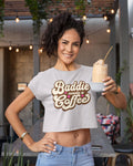 Woman wearing a 'Baddie needs a coffee' shirt holding a drink.
